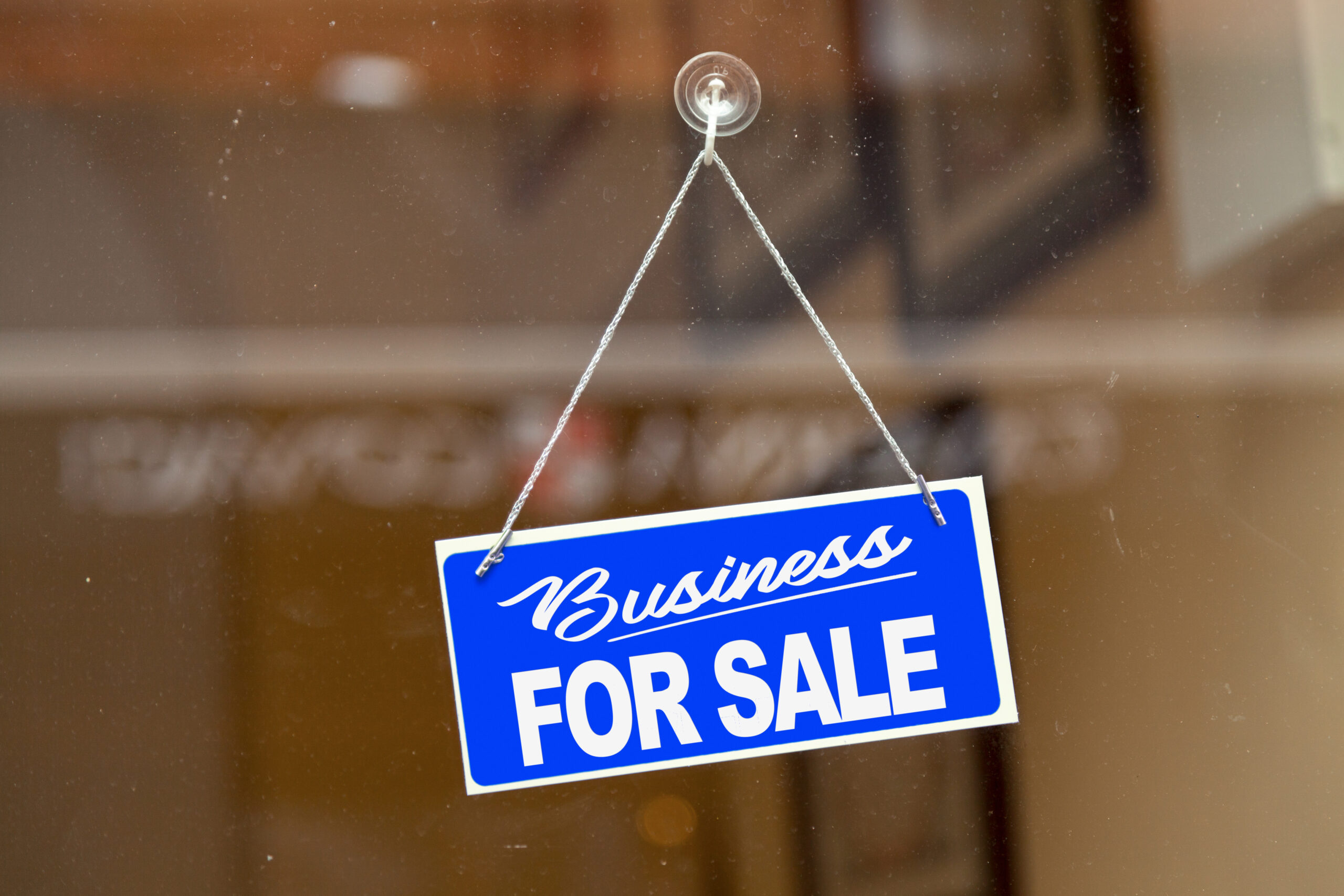 Blue sign hanging at the glass door of a shop saying: "Business for sale".