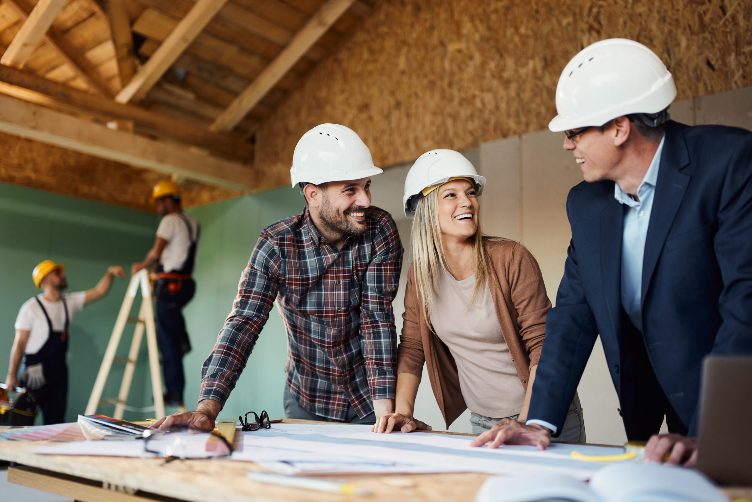 Happy couple and their real estate developer communicating while analyzing housing plans at construction site.